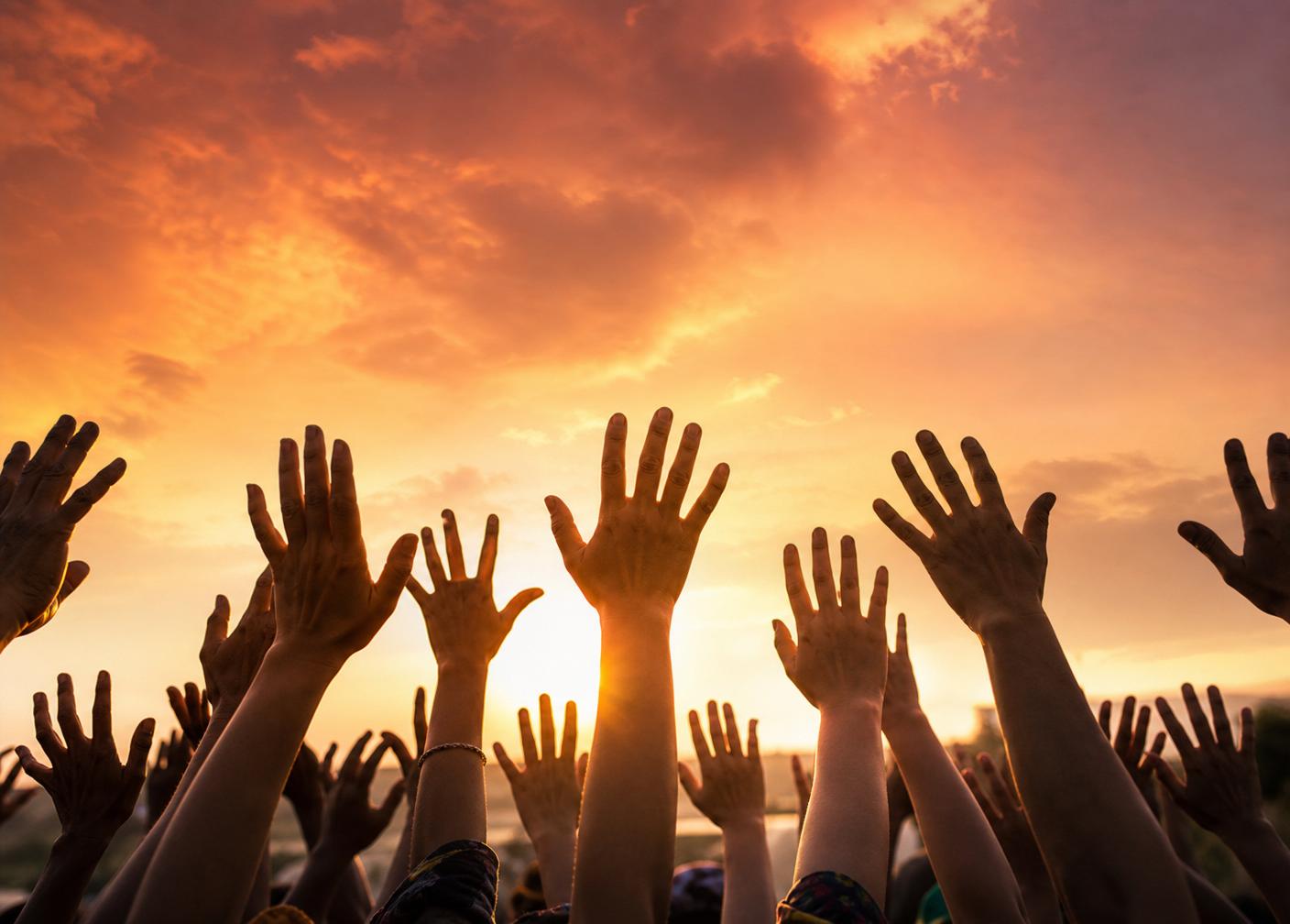 Many hands reaching upward together against a brilliant orange sky — a symbol of hope, unity, and human potential